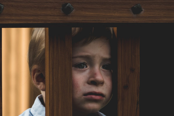 Kind mit traurigem Blick hinter Stäben